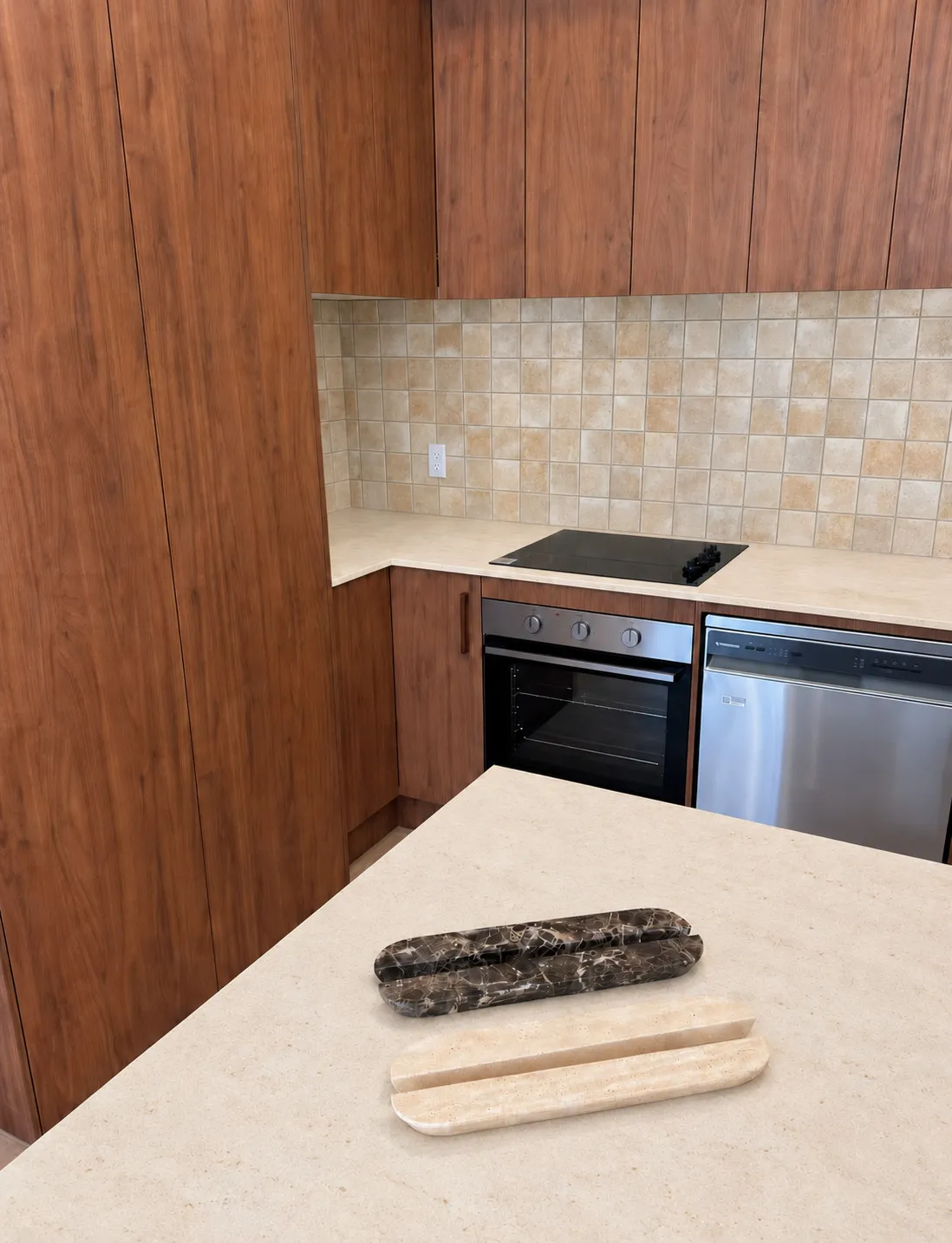 Two Oval Pulls on a pale stone counter, one in brown Emperador and one in cream Travertine Bianca, walnut cabinets behind